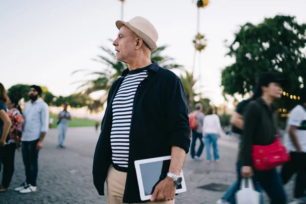 Moda giyinmiş Kafkas erkek blogcu emeklilik gününde modern dokunmatik pedi tutuyor ve yürüme zamanı gözlerini kaçırıyor. 60 'lı yaşlarda yakışıklı turist tek kişilik seyahatler sırasında dijital aletlerle düşünüyor.