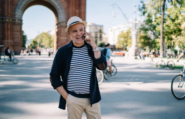 Saman şapkalı mutlu Kafkasyalı tek kişilik tatillerde uluslararası arama için gezinen internet bağlantısını kullanıyor, seyahat sırasında gülümseyen erkek turist gezici sohbetin keyfini çıkarıyor