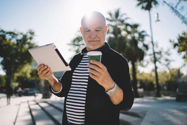 拥有现代触摸板的白种人大四 在外卖杯上浏览品牌信息 年长的博主60多岁 手持数字平板电脑 手握咖啡 整天呆在城市街道上 — 图库照片