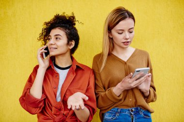 Hayalci kadın, dişlek tebessümü ile başka tarafa bakıyor ve dalgın bayan arkadaşının yanında akıllı telefondan konuşuyor sosyal ağları kontrol etmek için telefonu kullanıyor.