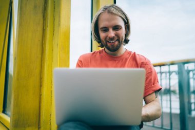 Neşeli, güler yüzlü, günlük giysiler içinde genç bir erkek arkadaşla sosyal medya mesajlaşması yaparken üstü kapalı yaya köprüsünde dizüstü bilgisayar kullanıyor.