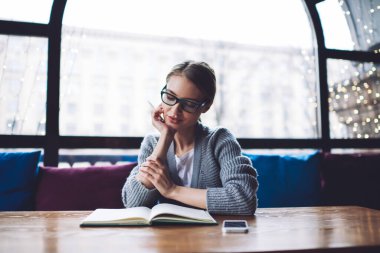 Elinde gözlüklerle oturmuş kitap okuyup boş zamanlarında kitap okuyan düşünceli bir kadın.