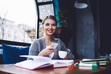 Kahve molası sırasında masada otururken ve cep telefonlarını karıştırırken günlük kıyafetlerini giymiş neşeli genç kız öğrenci gözlerini kaçırıyor.