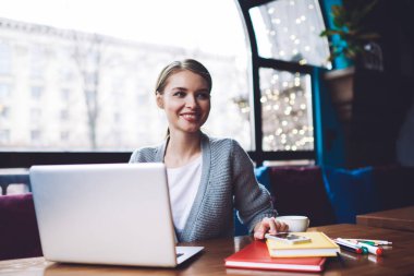 Genç, mutlu, uzaktan kumandalı bir kadın bilgisayar başında oturmuş akıllı telefon ekranına dokunurken gözlerini kaçırıyor.