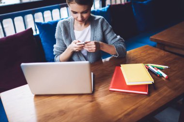 Gündüzleri kafede çalışırken akıllı telefon kullanan, elinde defterler ve netbook ile masada oturan, günlük giysiler içinde konsantre kadın girişimci.
