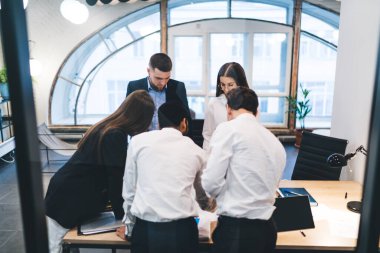 Yukarıdan gelen yoğun meslektaşlar masanın etrafında toplanıyor ve pencereli çağdaş ofiste birlikte çalışırken iş toplantıları yapıyorlar.