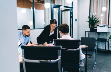Bir grup zeki genç iş arkadaşı resmi giysiler içinde masanın etrafında toplanıp fikirleri paylaşırken modern ofiste iş planlarını tartışıyorlar.