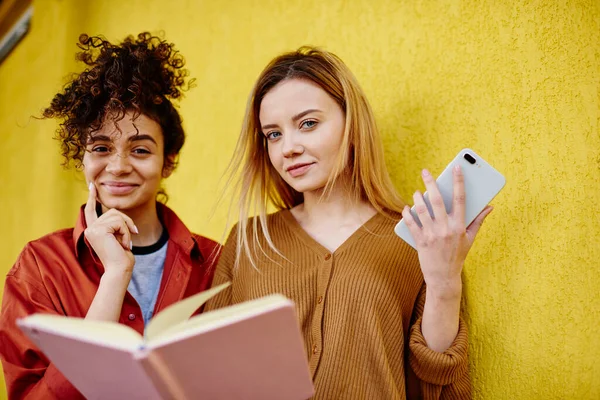 Smiling Young Female Friends Casual Wear Looking Camera While Reading — Stock Photo, Image