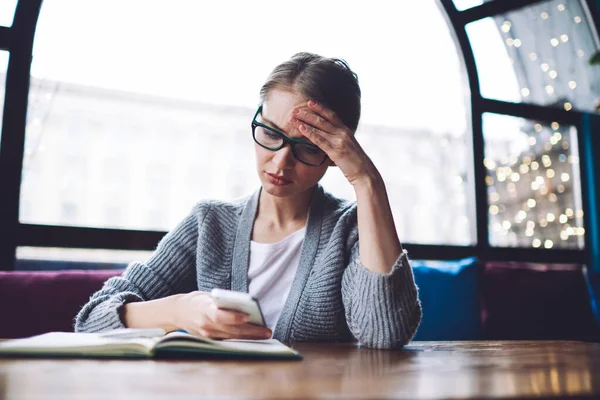 Serious Female Student Eyewear Gathered Hair Sitting Table Leaning Hand — стоковое фото