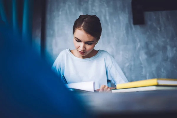 勉強中にメモ帳をテーブルに座り 紙に情報を書いているカジュアルな服を着た女子大生 — ストック写真