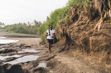 Yazın dalgalı deniz kıyısında sırt çantalı ve güneş gözlüklü, tanınmayan bir adamın vücudu.