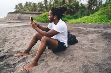 Mutlu Afro-Amerikan erkek turist günlük giysiler içinde tatil köyünde dinlenirken cep telefonuyla gülümsüyor ve konuşuyor.
