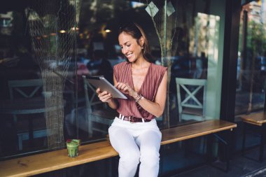 Modayı takip eden neşeli beyaz kadın boş zamanlarında dışarıda dinleniyor dijital tablet üzerinden mesaj yolluyor, güzel bir kadın posta kontrol ediyor ve dışarıda iletişim kuruyor.