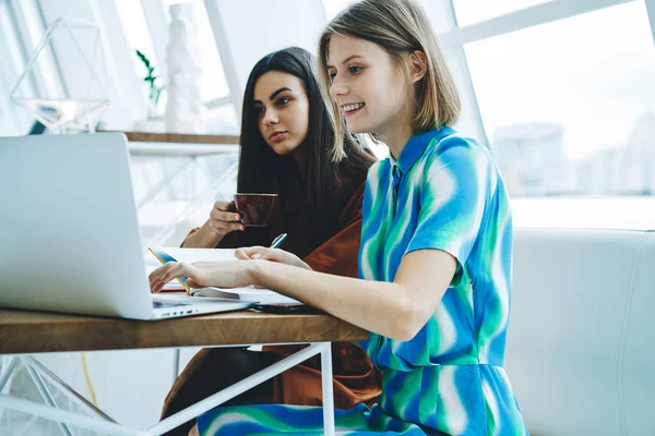 集中注意力的年轻女性在咖啡馆里坐在桌边 白天边喝咖啡边用电脑和在笔记本上写笔记 — 图库照片