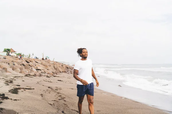 夏の晴れた日に海を振って近くの砂浜を歩いている間 スポーツウェアを着た深刻なアフリカ系アメリカ人スポーツマン — ストック写真