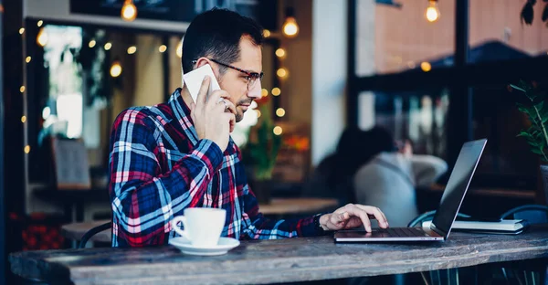 Millennial Man Working Freelance Using Modern Laptop Device While Talking — стоковое фото