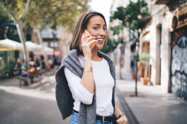 Mükemmel gülüşü olan dişlek kadın turistin yarım boy portresi modern cep telefonu cihazıyla uluslararası olumlu sohbetler sırasında seviniyor, gezici bağlantıyı konuşmak için kullanan neşeli kız.