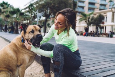 Mutlu Kafkasyalı fit kız, deniz kıyısındaki kardiyo antrenmanından sonra dinlenen, yürüyüş ve antrenman için boş zamanlarının tadını çıkaran beyaz köpekle eğleniyor.