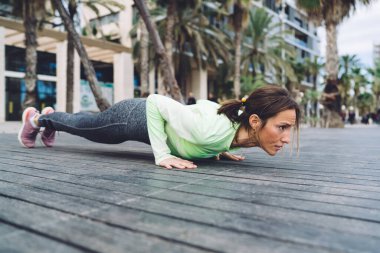 Tam vücut yetişkin fitness eğitmeni çok katlı bina ve avuç içlerinin yanındaki tahta zeminde şınav çekiyor.