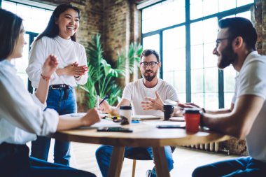 Bir grup başarılı genç girişimci takım çalışması brifingi için işbirliği içinde beyin fırtınası yapmaktan zevk alıyor, çeşitli hipster adamlar içeride öğrenim görmek için birlikte araştırma yaparken gülümsüyorlar.