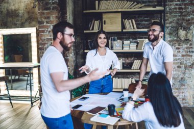 Modern ofisteki beyin fırtınası sırasında yeni iş projesiyle ilgili iletişim kurarken gündelik giysiler içinde gülümseyen mutlu genç iş arkadaşları.