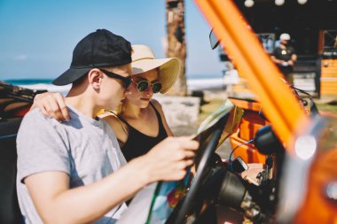 Arabada oturup, yaz gününün tadını çıkarırken haritaya bakan düşünceli çiftin yan görüntüsü.
