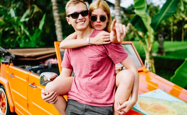 Tranquil Female Traveler Sunglasses Hugging Smiling Boyfriend Pointing Away While — стоковое фото