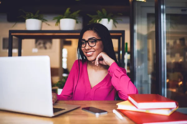 Szczęśliwa Afroamerykanka Warkoczami Luźnych Ubraniach Okularach Patrząc Ekran Laptopa Podczas — Zdjęcie stockowe