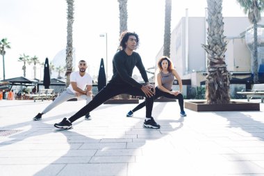 Arkadaki çok ırklı sporculardan oluşan tüm vücudun altından şehir meydanındaki açık havada antrenman sırasında sağa sola salınan bir grup.