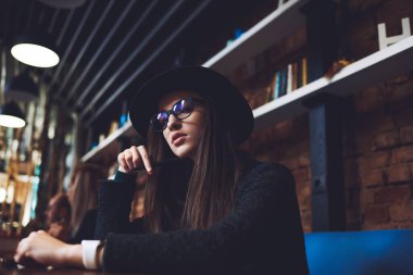 Kafeteryadaki masada oturup düşünürken şapkalı, sıradan siyah elbiseli ciddi bir kadının alçak açısı.