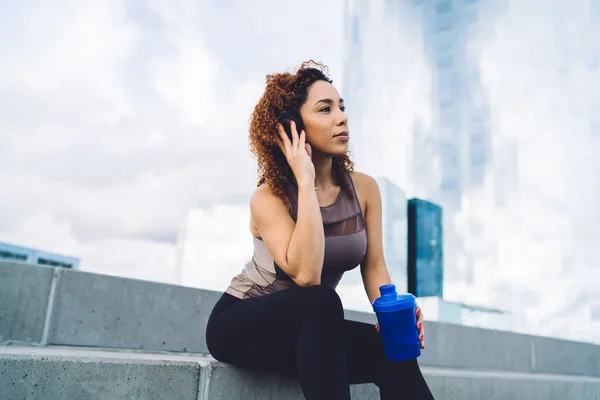 Sporty Ethnic Woman Bottle Water Sitting Stairs Urban Environment Listen — Stockfoto