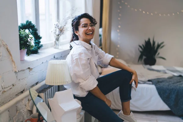 Smiling Female Smartphone Hand Eyeglasses Looking Camera While Sitting Shelf — Fotografia de Stock