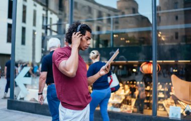 Bluetooth kulaklıklı milenyum hipster 'lı adam, şehirde boş zamanlarında müzik çalma listesi dinliyor, dijital tabletli şaşkın erkek blogcu, internet sitesinden müzik podcast' i seçiyor.