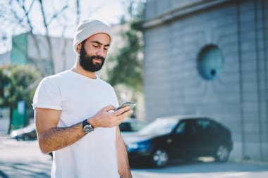 Türk erkek turist İnternet sitesinde 4G İnternet bağlantısı kullanan tatiller hakkında çevrimiçi bilgi kontrolü yapıyor, moda şapka giyen Orta Doğulu hippi medya metni yayınları okuyor