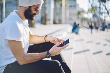 Milenyum sakallı adam sosyal ağlarda akıllı telefon sohbetleri sırasında mektup yazıyor. Modern mobil cihazlarda 4G kablosuz bağlantı kullanıyor. Ortadoğulu hippi adam şehirde tatil yayınlarını okuyor.