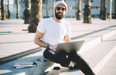 Modern netbook 'u olan Türk dijital göçebesi serbest çalışma sırasında şehir merkezinde günlerini web projeksiyonu için harcıyor, dışarıda dizüstü bilgisayarla poz veren sakallı hippi portresi yapıyor.