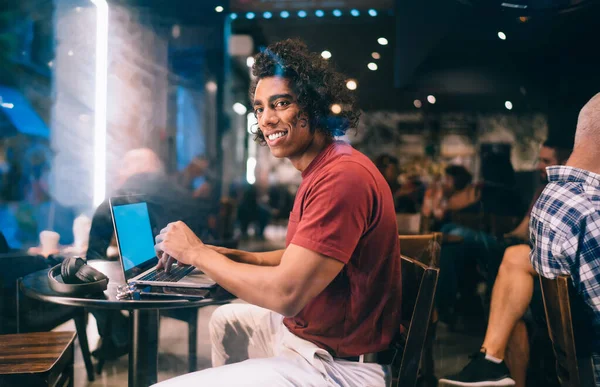 Gülümseyen serbest çalışan erkek, kafeteryada oturup modern dizüstü bilgisayar teknolojisi üzerinde mesai yapıyor. Günlük kıyafetleri giyen mutlu blogcu, netbook bilgisayar kullanarak kahve dükkanında çalışıyor.