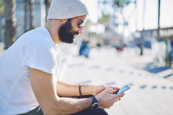 Turkish travel blogger phoning for cellphone chatting with network followers using roaming internet during vacations, bearded hipster guy in sunglasses browsing website via mobile technology