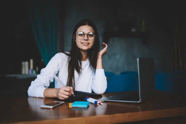 Smiling Young Brunette Eyeglasses Wearing Casual Clothing Sitting Wooden Desk — Fotografia de Stock