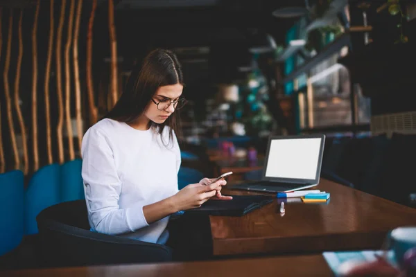 Pensive Female Freelancer Sitting Table Opened Laptop Using Smartphone While — Stock fotografie