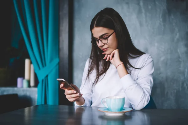 Pensive Female Повсякденному Вбранні Окулярами Сидячи Столом Чашкою Чаю Спирається — стокове фото