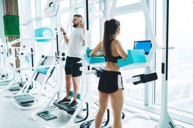 Uzun saçlı atletik sporcu kadın yoğun antrenman sırasında modern ferah spor salonunda spor aletlerinin yanında spor aletleri üzerinde egzersiz yapıyor.