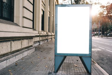 Otobüs durağının yanında, soğuk mevsimde güz ağaçlarına ve parlak güneş ışığına karşı modern şehir sokaklarının boş beyaz tabelası.