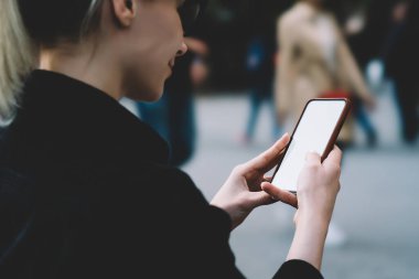 Gündüz vakti şehir caddesinde cep telefonuyla mesajlaşırken ekranda güneş gözlüğü takan pozitif genç bir kadın.