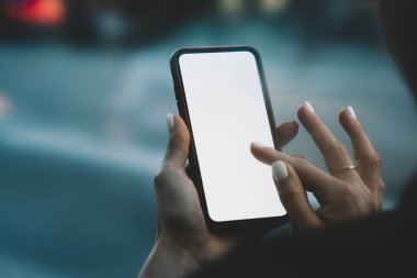 Manikürlü elleri ve parmağında yüzüğü olan, şehirde dikilen ve iş sırasında telefondaki boş ekrana bakan bir kadın.