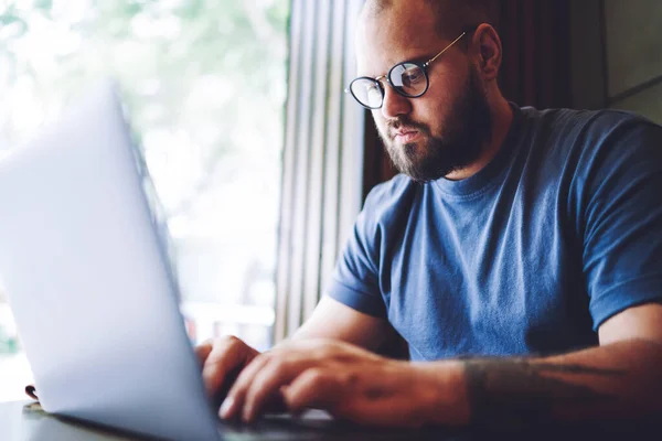 Crop Concentrated Bearded Male Casual Clothes Eyeglasses Sitting Table Window — Zdjęcie stockowe