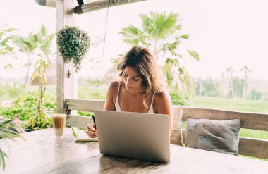 Genç, etnik, uzaktan kumandalı kadın çalışan. Kafedeki terasta netbook ve bir bardak kahveyle günlüğe not alıyor.