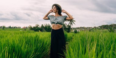 Yeşil çayır boyunca tek başına yürürken ve kırsalda özgürlüğün tadını çıkarırken rahat bir şekilde giyinen esmer kadın.