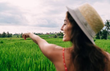 Bali 'deki yaz gezisi sırasında yeşil alanda gezinirken ileri ve geri bakan modaya uygun şapkalı kadın gezginin arka görüntüsü
