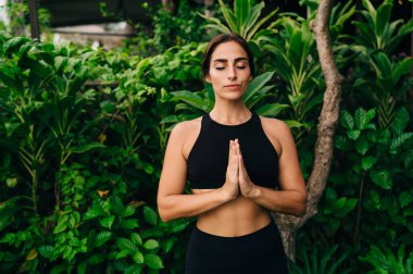 Namaste poziyonunda 30 'lu yaşlarda sakin bir kadın sabah meditasyonu sırasında dua ederken, siyah spor giyim giymiş beyaz kadın yogi dikkatle dinlenmek için dinlenirken ruh uyumunu hisseder.